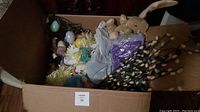 Box filled with Easter decorations including plush bunny, decorative eggs, and floral stems.