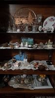 Photo of wooden shelves filled with assorted decorative glassware, ceramics, figurines and collectibles on lace doilies.