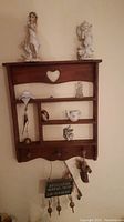 Wooden heart cutout wall shelf with various small porcelain and metal figurines and a hanging inspirational plaque