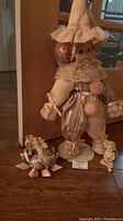 Clown doll standing with decorative shoe and dog figurine on wood floor in front of mirror