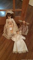 Porcelain doll in lace dress standing, two fabric angel dolls lying and standing around it