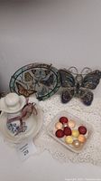 Photo of decorative butterfly glass plate, stained glass butterfly, ceramic pitcher and basin, and glass dish with poker chips on lace cloth.