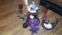 Photo showing all items on wooden floor including purple vase, glass bowl with seashells, purple star ornament, glass orb, and metal flower sculpture