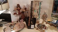 View of metal jewelry holder shaped like woman sitting at table, black velvet display bust with gold-tone bracelets and earrings, cream multi-hook jewelry tree with hanging earrings and necklaces, and silver tray with glass perfume bottles and assorted costume jewelry.