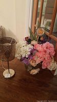 Decorative lamp with metal patterned shade and white base beside clear glass vase filled with artificial flowers including pink, white, purple, cream colors