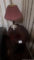 View of oval wooden table with red and brass table lamp placed on top.