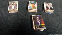 Four groups of baseball cards stacked and spread out, showing a variety of players and card designs. Mostly baseball cards with different years and brands.