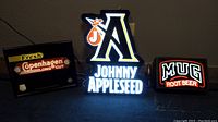 Photo showing all three vintage light box advertising signs illuminated: MUG Root Beer, Johnny Appleseed, and Copenhagen Long Cut Chewing Tobacco