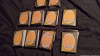 Ten stacks of Magic the Gathering cards, face down, showing the backs with Magic logo, arranged on a black fabric surface.