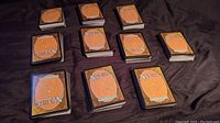 Overview of ten stacks of Magic the Gathering collectible cards arranged on a black cloth surface showing card backs with classic design.