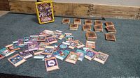 Yu-Gi-Oh! cards scattered on surface with some organized stacks and yellow themed tin visible in background