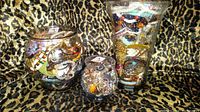 Three glass jars filled with assorted vintage jewelry including colorful necklaces, bracelets, rings, pins, and brooches displayed on leopard print fabric.