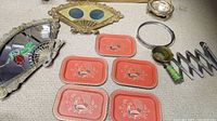 Lot arranged on carpet showing five orange metal trays, brass fan-shaped picture frames, and miscellaneous metal items including mirror frame and expandable rack.