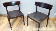 Pair of Mid-Century Modern style wood chairs with dark brown finish against a light grey wall.