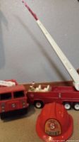 Side view of vintage Tonka metal fire truck with extendable white ladder and Mattel plastic truck. Red Fisher Price fire chief hat in front.