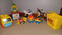 Photo showing the full assortment of vintage toys from the lot including the Fisher Price train and cars, Jack in the Box clown, miniature horse tricycle, winged horse toy, and yellow Wizard of Oz basket.