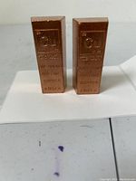 Two 1 pound copper bars standing upright showing front engraved details including element symbol, weight, purity and country of origin.