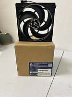 Single ARCTIC P12 PWM PST 120mm Fan on top of the brown box showing fan blades and frame design