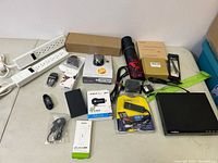 Overview of lot showing various electronic accessories including power strips, USB dongles, remote controls, cables, and boxed items