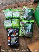 Photo showing multiple bags of fertilizer and lawn care products on a wooden pallet, including tree and hedge fertilizer and vegetable and herb mix.