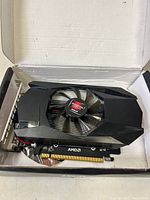 Front view of the AMD HD7670 graphics card with cooling fan and PCIe connection in its box.