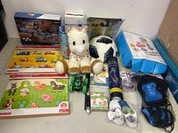 Lot overview showing various toys and games: plush giraffe, soccer ball, puzzles, toy vehicles, boxed games, and sports equipment.