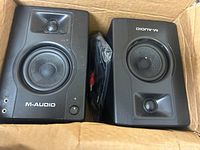 Pair of M-Audio BX3 multimedia monitors inside a cardboard box, showing front view of speakers