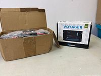 Open cardboard box containing the solar charge controller and accessories in plastic packaging, placed on a white surface.