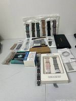 Full lot of assorted new watch bands and accessories spread on a table, including multiple packaged bands in different colors and patterns.