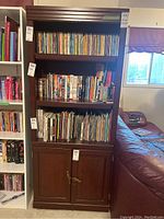 Front view of wood veneer bookshelf with three shelves filled with books and DVDs and closed lower cabinets with chained lock.