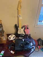 Original Xbox console with multiple cables and controllers on top including wired black controllers, memory cards, and guitar controller accessory shown.