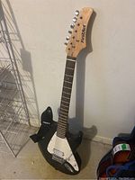 Black First Act electric bass guitar standing against wall, showing full front view with maple neck and rosewood fretboard.