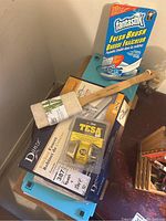 Photo of various household items including a Fantastik Fresh Brush, bamboo clothes folder, loofah, and Tesa deadbolt lock on top of a blue storage bin.