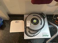iRobot Roomba vacuum and white bathroom scale placed on a counter or table.