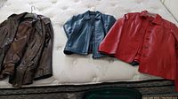 Three leather jackets laid out on a mattress: brown Beardmore, blue Danier, and red Danier.