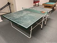Full view of green ping pong table with white folding metal legs and paddles on top, showing condition and size.