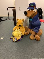 Scooby Doo plush, Winnie the Pooh plush, and Pokemon plush backpack grouped on floor for display