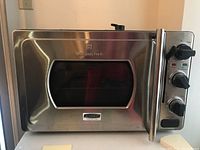 Front view of stainless steel Wolfgang Puck Kitchentek pressure oven showing rectangular window and handle.