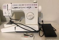 Full side view of the Singer sewing machine with foot pedal cable connected displayed on a table.