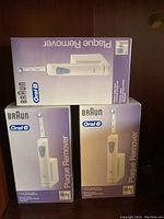 Three boxed Braun Oral-B Plaque Remover electric toothbrushes stacked on a surface, showing front and side views of the packaging