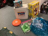 Overall photo showing boxed Workman Deluxe Tool Set, Tonka Fire Rescue Toy box, inflatable chairs, badminton items, pink butterfly net, and orange flying disc on carpet.