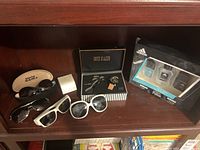 Photo shows a wooden shelf holding the Adidas gift set, the wristwatch in a black box, and four pairs of sunglasses, two black pairs, one white, and one in Eye Faker branded case.