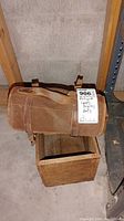 Brown canvas carrying bag with leather straps resting on wooden storage box in basement setting.