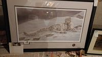 Front view of the framed and matted art print showing a snow leopard in a snowy environment, signed by Michael Page, with a certificate attached inside the frame.