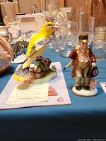 Yellow bird and man figurines displayed with glassware in the background
