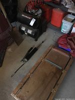 Motomaster air compressor, wooden creeper trolley, and grease gun on the floor with additional items around.