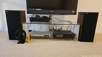 Full set up view showing two Paradigm speakers, Sony wireless headphones, flashlight, VHS player, Onkyo amplifier and DVD player under a TV stand.