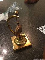 Gold pocket watch hanging on brass stand, front-left view