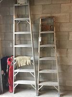 Photo showing both ladders standing side by side against cinder block wall with visible step design and size difference.