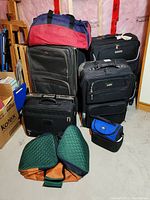 Photo showing multiple bags including two large black rolling suitcases, a medium suitcase, a red and blue duffle bag, a small blue and black bag, a green padded item, and a black briefcase.